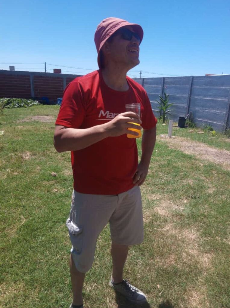 Foto hombre de remera roja y bermudas con gorro y lentes de sol.