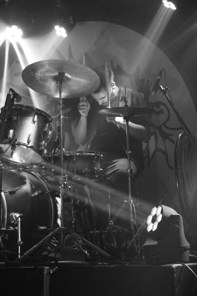 Persona tocando la batería en escenario, foto en blanco y negro.